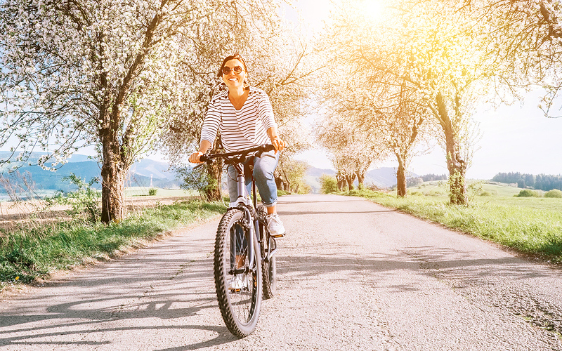 Happy smiling woman rides a bicycle on the country road under blossom trees. Spring is comming concept image.