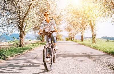 Happy smiling woman rides a bicycle on the country road under blossom trees. Spring is comming concept image.