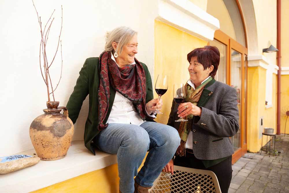 Zwei Frauen im Innenhof im Haus der Frauen stoßen mit einem Glas Rotwein auf die Freundschaft an